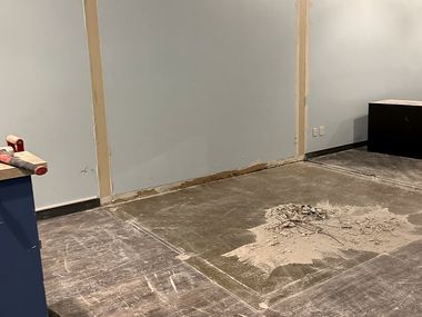 After: the same commercial unit cleared and swept — bare concrete floor, the wall scarred where a partition was removed, and a single small pile of dust left to sweep.